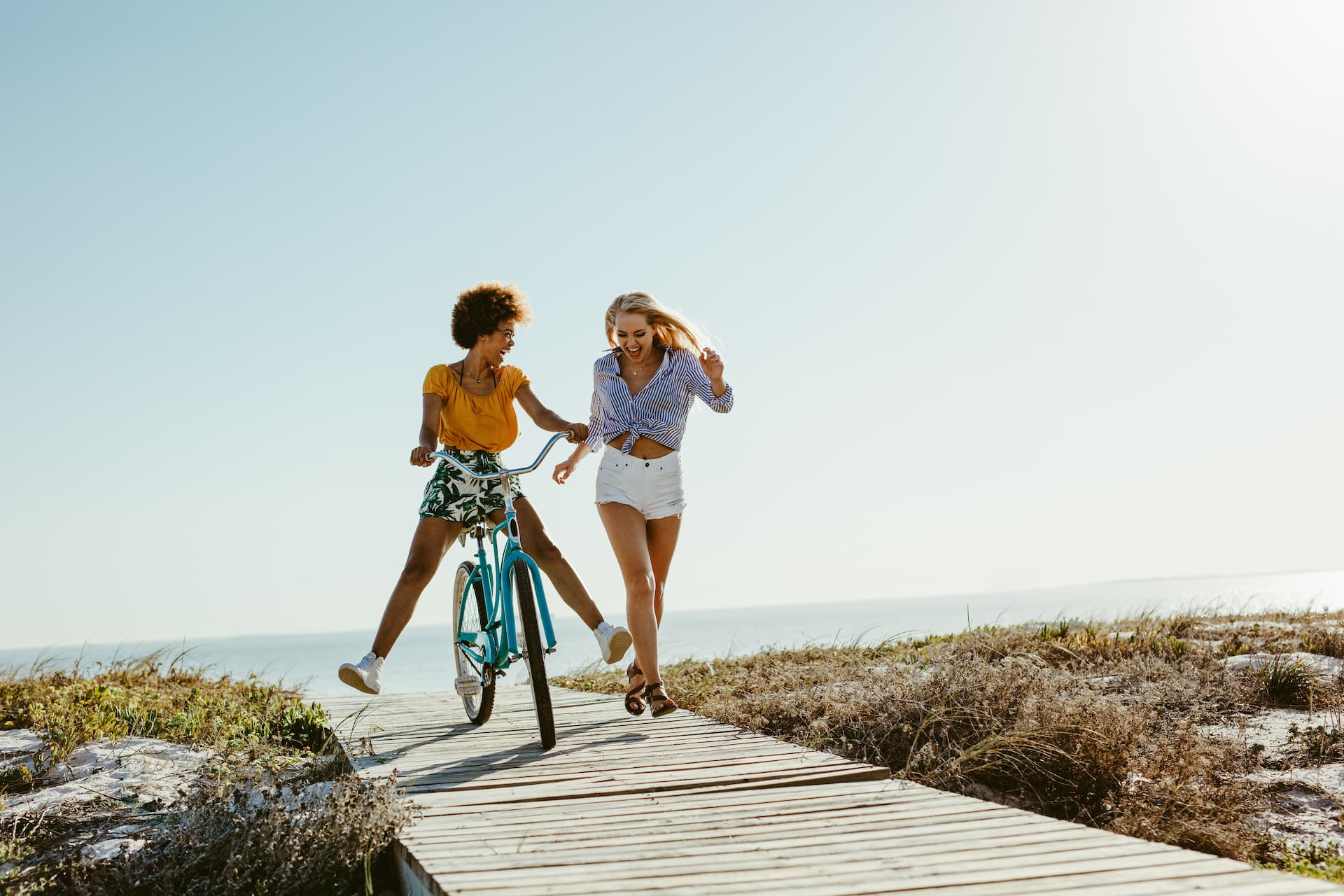 Two women laughing while walking on beach boardwalk